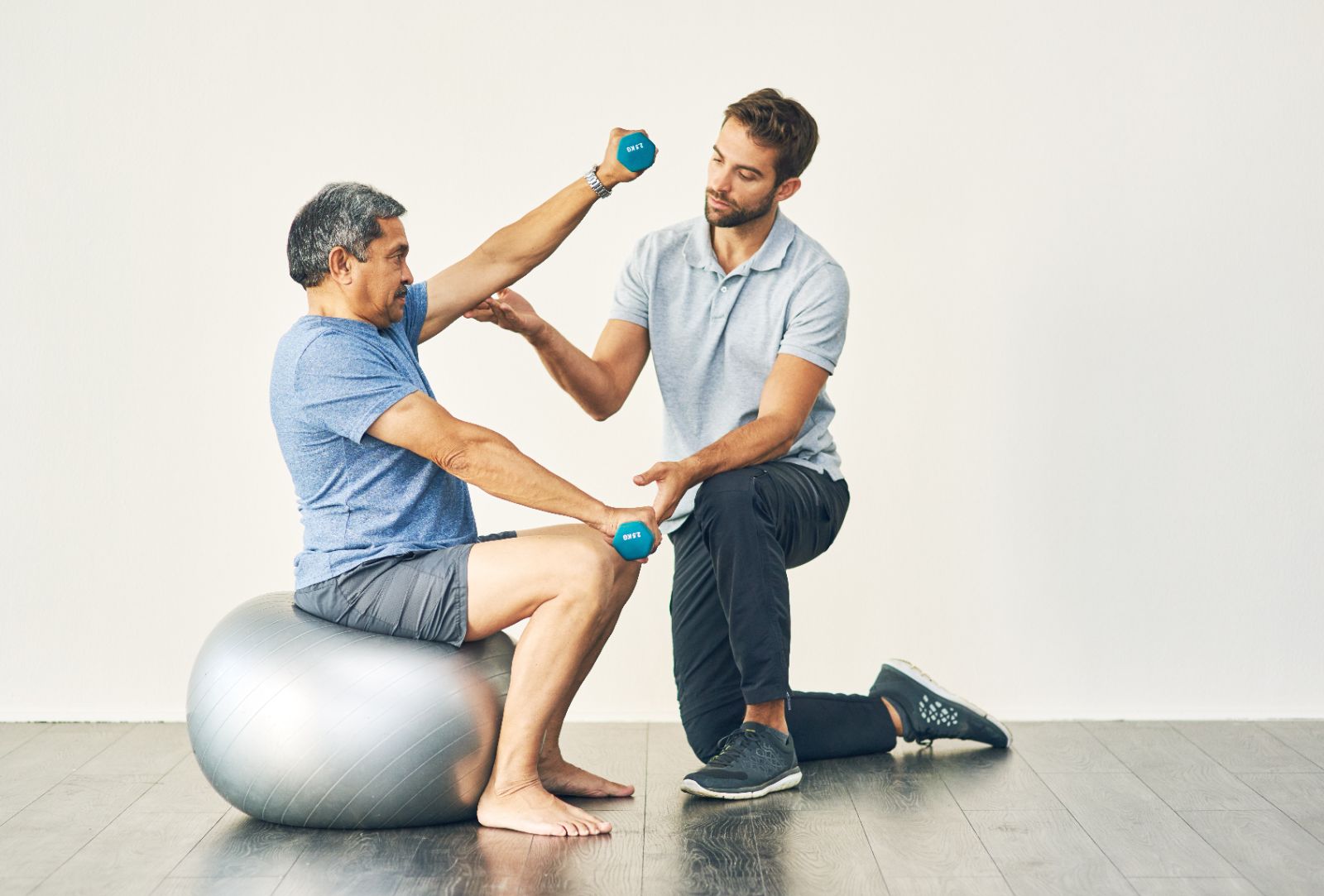 A physiotherapist guiding a patient through a dumbbell rehab exercise on a stability ball